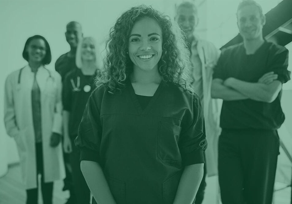 Smiling young female doctor standing in a hospital corridor with a diverse group of medical staff standing behind her